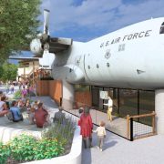 Architectural rendering of a US Air Force C-130 aircraft mounted above a zoo lion habitat, with visitors seated at an amphitheater below.