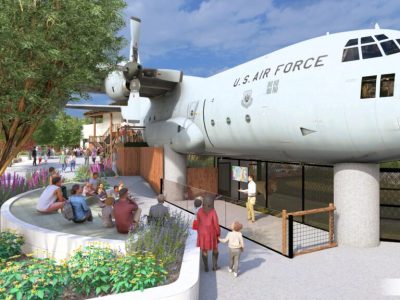 Architectural rendering of a US Air Force C-130 aircraft mounted above a zoo lion habitat, with visitors seated at an amphitheater below.