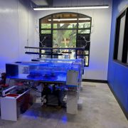 Rows of shallow coral propagation tanks lit blue sit on white benches inside the Brewer Ocean Conservation Lab, with guests visible through an arched window.