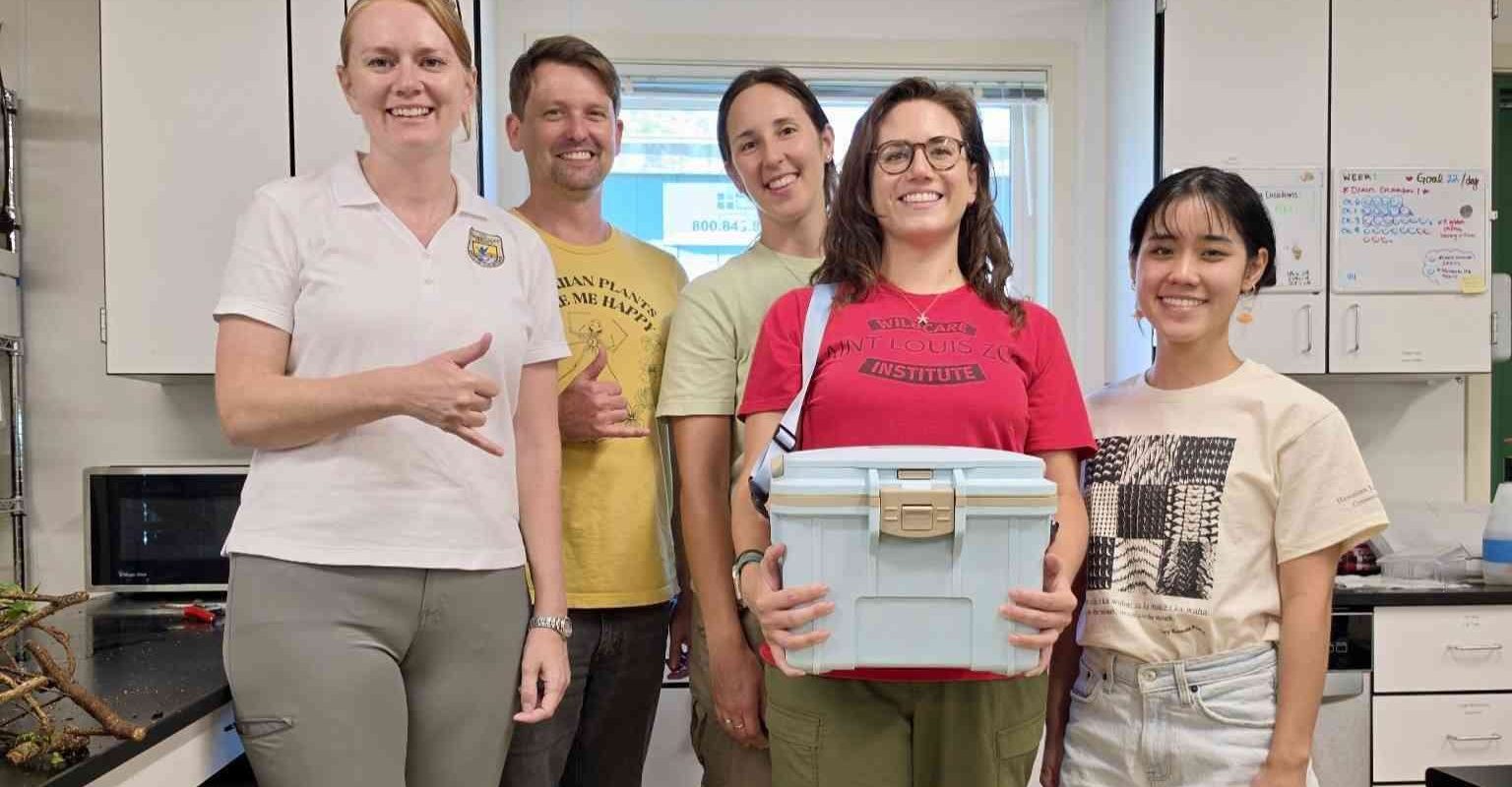 Five staff members stand together in a laboratory, one holding a white transport cooler containing rescued snails.