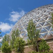 The geodesic Desert Dome at Omaha's Henry Doorly Zoo and Aquarium rises above trees against a blue sky.