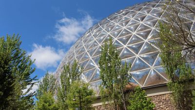 The geodesic Desert Dome at Omaha's Henry Doorly Zoo and Aquarium rises above trees against a blue sky.