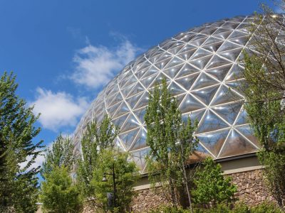The geodesic Desert Dome at Omaha's Henry Doorly Zoo and Aquarium rises above trees against a blue sky.
