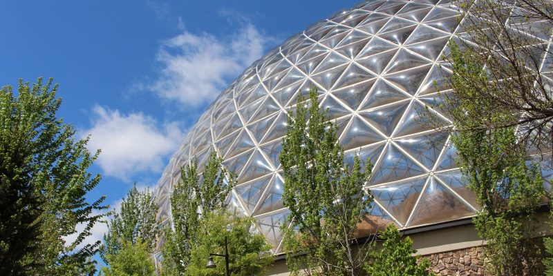 The geodesic Desert Dome at Omaha's Henry Doorly Zoo and Aquarium rises above trees against a blue sky.