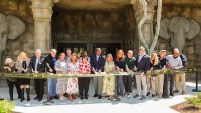 A long line of people cut a ribbon in front of the stone elephant-head facade of Tulsa Zoo's renovated elephant building.
