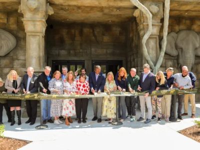 A long line of people cut a ribbon in front of the stone elephant-head facade of Tulsa Zoo's renovated elephant building.