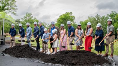 A line of people in hard hats hold gold shovels over a mound of soil at the Memphis Zoo groundbreaking for Stingrays at Mangrove Cove.