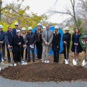A row of people in white hard hats hold gold shovels over a mound of soil at the Wild Iowa groundbreaking, autumn trees behind them.