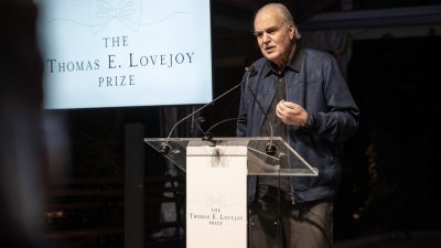 Dr. Carlos Afonso Nobre speaks at a clear lectern beside a screen reading The Thomas E. Lovejoy Prize above a line drawing of a bow tie.