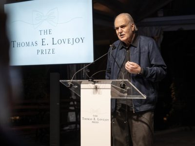 Dr. Carlos Afonso Nobre speaks at a clear lectern beside a screen reading The Thomas E. Lovejoy Prize above a line drawing of a bow tie.