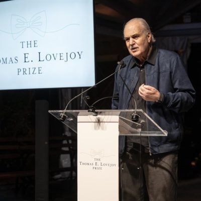Dr. Carlos Afonso Nobre speaks at a clear lectern beside a screen reading The Thomas E. Lovejoy Prize above a line drawing of a bow tie.