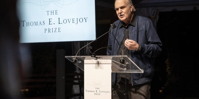 Dr. Carlos Afonso Nobre speaks at a clear lectern beside a screen reading The Thomas E. Lovejoy Prize above a line drawing of a bow tie.