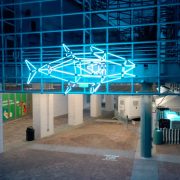 A large illuminated sculpture shaped like a tuna glows against a dark city street outside the entrance to Audubon Aquarium, its surface lit in shifting colors.