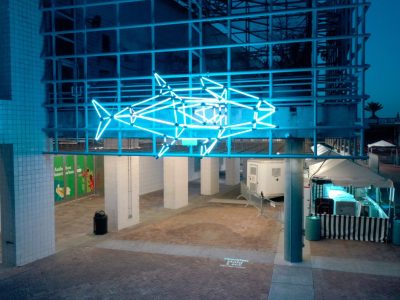 A large illuminated sculpture shaped like a tuna glows against a dark city street outside the entrance to Audubon Aquarium, its surface lit in shifting colors.