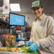 A Disney cast member slicing fruit beside a screen showing an animal diet plan