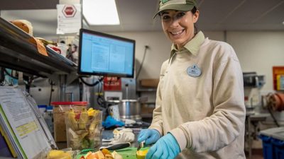 A Disney cast member slicing fruit beside a screen showing an animal diet plan