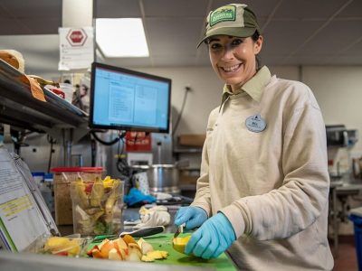 A Disney cast member slicing fruit beside a screen showing an animal diet plan