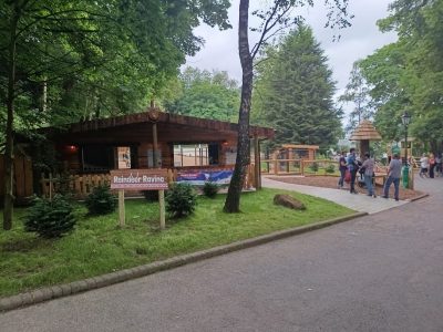 A timber lodge and paddock behind a sign reading Reindeer Ravine, with visitors walking along a path.