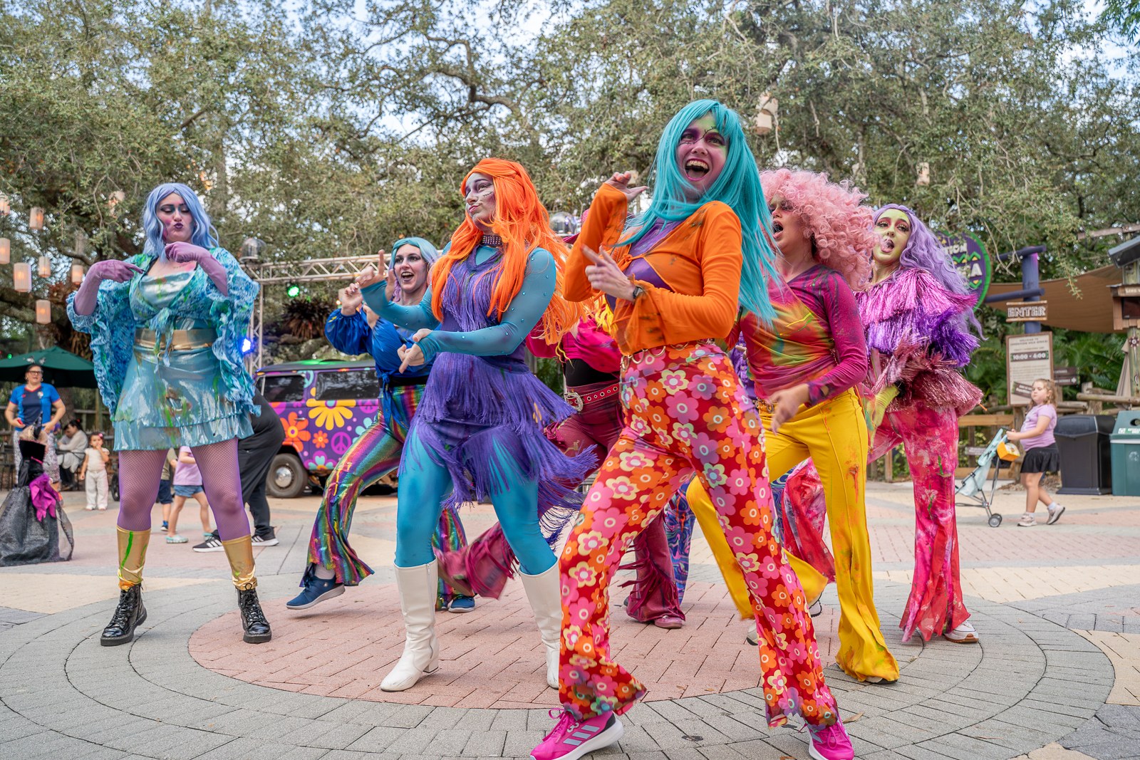 Performers in bright wigs and 1970s outfits dancing on a paved circle at ZooTampa during Creatures of the Night