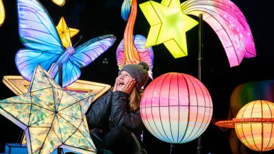 A child in a woolly hat sitting among lit star, planet, butterfly and flamingo lanterns at night