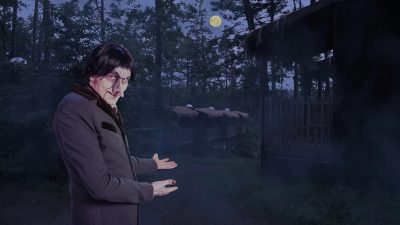A pale, gaunt undertaker character in a long gray coat gestures toward wooden cabins in a misty moonlit forest.