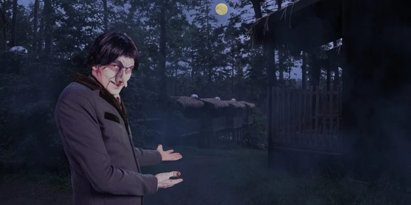 A pale, gaunt undertaker character in a long gray coat gestures toward wooden cabins in a misty moonlit forest.