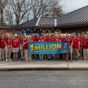A large group of volunteers in red shirts stands outside a zoo building holding a banner reading Celebrating 1 Million Volunteer Hours.