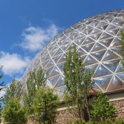The glass geodesic roof of the Desert Dome at Omaha's Henry Doorly Zoo and Aquarium rises above green trees under a blue sky.