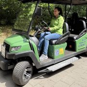 A zoo staff member sits at the wheel of a small green electric vehicle with an open side and a boarding ramp.
