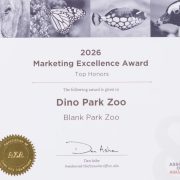 An award certificate printed with a row of animal photographs along the top, reading 2026 Marketing Excellence Award, Top Honors, given to Dino Park Zoo, Blank Park Zoo, with a gold Association of Zoos and Aquariums seal and the signature of Dan Ashe.