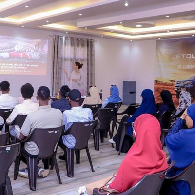 Rows of students sit facing a Cheetah Conservation Fund veterinarian who is presenting beside a projected slide reading, when an animal gets sick, is the problem only about that one animal, in a classroom at the CCF Somaliland campus near Hargeisa.