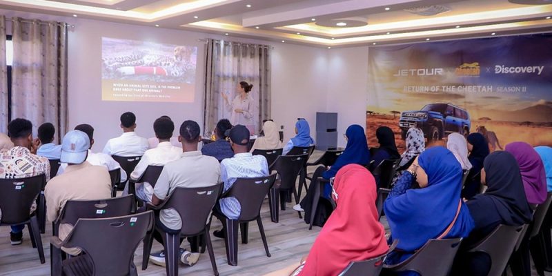 Rows of students sit facing a Cheetah Conservation Fund veterinarian who is presenting beside a projected slide reading, when an animal gets sick, is the problem only about that one animal, in a classroom at the CCF Somaliland campus near Hargeisa.