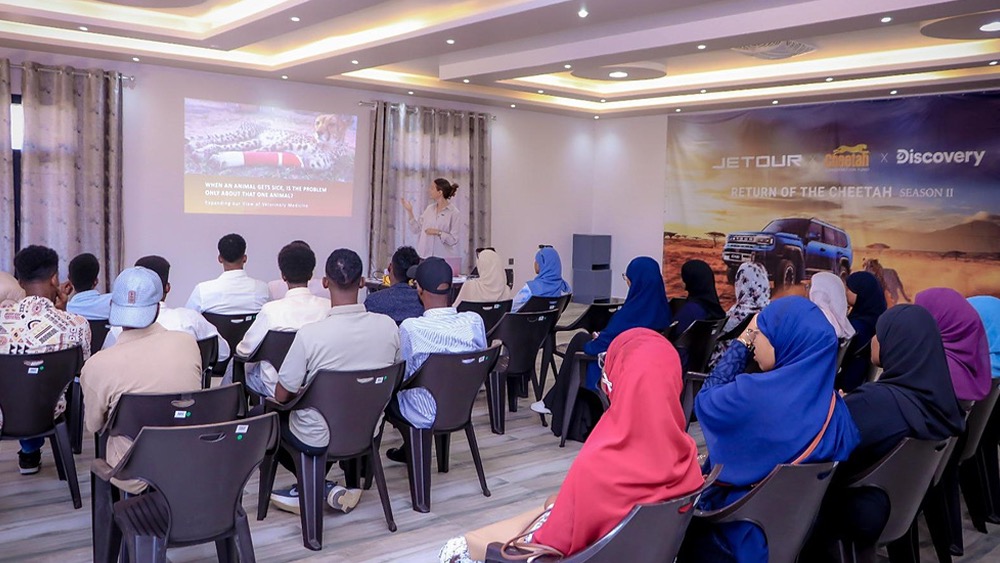 Rows of students sit facing a Cheetah Conservation Fund veterinarian who is presenting beside a projected slide reading, when an animal gets sick, is the problem only about that one animal, in a classroom at the CCF Somaliland campus near Hargeisa.