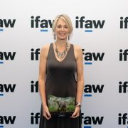 Rachael Murton stands holding a framed IFAW Animal Action Award showing a photograph of an elephant, in front of a wall printed with the IFAW logo.