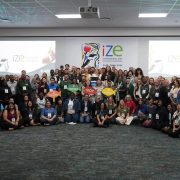 A large group of conference delegates stands and crouches together for a group photograph in front of a screen reading IZE International Zoo Educators Conference Cape Town 2026.
