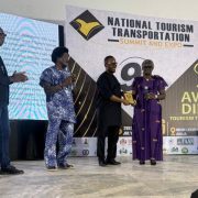 A Lekki Conservation Centre representative accepts a gold award plaque on stage at the National Tourism and Transportation Summit awards night in Abuja, Nigeria.