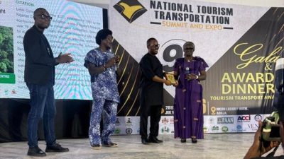 A Lekki Conservation Centre representative accepts a gold award plaque on stage at the National Tourism and Transportation Summit awards night in Abuja, Nigeria.