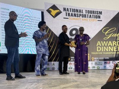 A Lekki Conservation Centre representative accepts a gold award plaque on stage at the National Tourism and Transportation Summit awards night in Abuja, Nigeria.