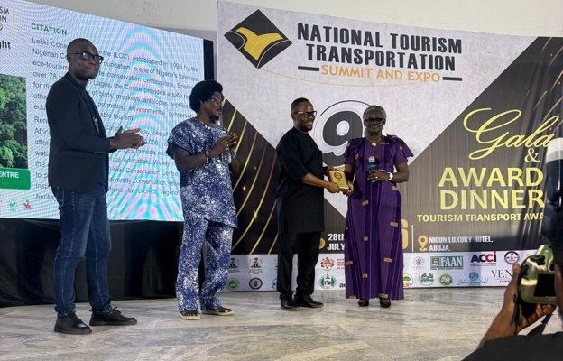 A Lekki Conservation Centre representative accepts a gold award plaque on stage at the National Tourism and Transportation Summit awards night in Abuja, Nigeria.