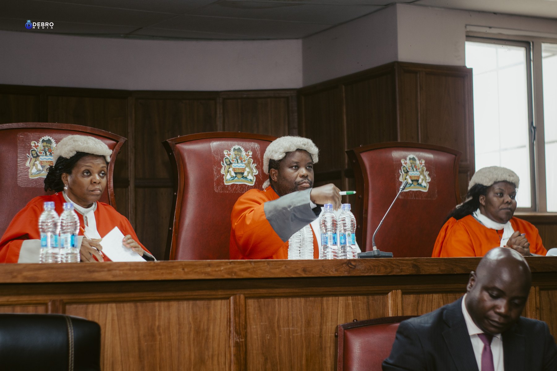 Three judges in scarlet robes and wigs sit at the bench beneath the Malawi coat of arms.
