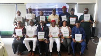Thirteen delegates pose in two rows at the Abuja launch of Nigeria's National Business Action Plan for Biodiversity, each holding a printed copy of the plan, in front of a banner reading strengthening business engagement in Nigeria's biodiversity agenda.