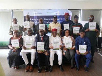 Thirteen delegates pose in two rows at the Abuja launch of Nigeria's National Business Action Plan for Biodiversity, each holding a printed copy of the plan, in front of a banner reading strengthening business engagement in Nigeria's biodiversity agenda.