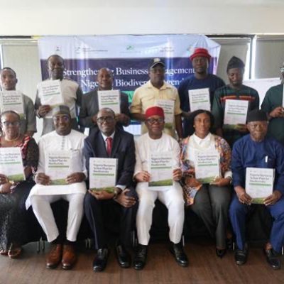 Thirteen delegates pose in two rows at the Abuja launch of Nigeria's National Business Action Plan for Biodiversity, each holding a printed copy of the plan, in front of a banner reading strengthening business engagement in Nigeria's biodiversity agenda.