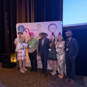 Palm Beach Zoo staff stand together in novelty hats in front of a Nonprofits First backdrop after accepting the Hats Off award, one of them holding the award box.
