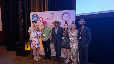 Palm Beach Zoo staff stand together in novelty hats in front of a Nonprofits First backdrop after accepting the Hats Off award, one of them holding the award box.