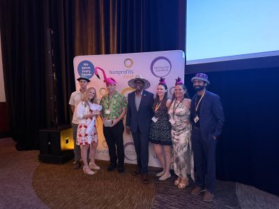 Palm Beach Zoo staff stand together in novelty hats in front of a Nonprofits First backdrop after accepting the Hats Off award, one of them holding the award box.