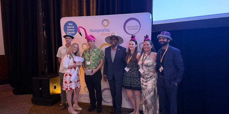 Palm Beach Zoo staff stand together in novelty hats in front of a Nonprofits First backdrop after accepting the Hats Off award, one of them holding the award box.